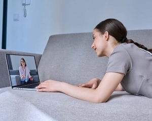 A teenage girl is lying on a sofa at home, participating in an online therapy session with a counsellor. An example of counselling in Edmundston, representing a virtual counselling session.